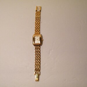 May include: A gold-toned wristwatch with a square face and a gold metal band.