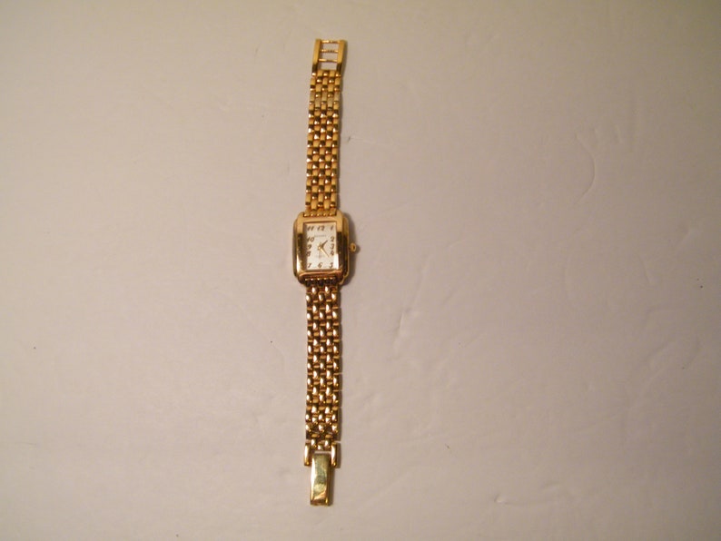 May include: A gold-toned wristwatch with a square face and a gold metal band.