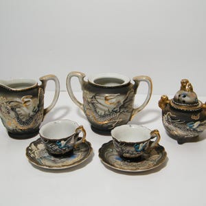 Peut inclure: Un service à thé en porcelaine noire et dorée avec un pot à crème, un sucrier, deux tasses et soucoupes et un brûle-encens.