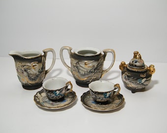 Könnte beinhalten: Ein schwarzes und goldenes Drachen-Tee-Set mit Milchkännchen, Zuckerdose, zwei Teetassen und Untertassen sowie einem Räuchergefäß.