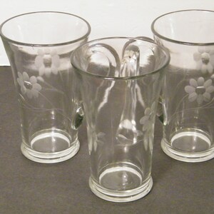 May include: Three clear glass mugs with etched floral designs. The mugs have a rounded bottom and a flared top.