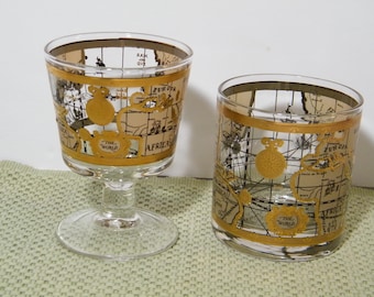 May include: Two vintage drinking glasses with gold trim and a world map design. The glasses are on a green placemat.