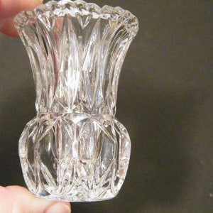 May include: A clear glass bud vase with a cut glass design. The vase has a wide mouth and a narrow base.