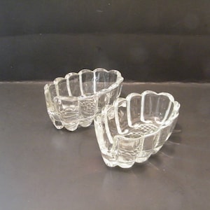 May include: Two clear glass bowls with a fluted design. The bowls are shaped like hearts and have a scalloped edge.