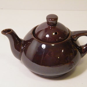 May include: A small brown ceramic teapot with a lid and a spout. The teapot has a round body and a handle.