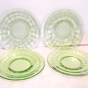 May include: Four glass plates in the image. Two are clear with concentric circle designs, and two are a light green color with similar concentric circle designs. The plates are arranged in a square formation.