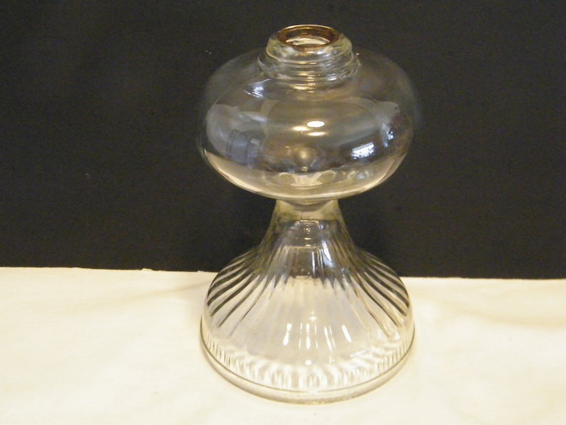 May include: A clear glass oil lamp with a round, ribbed base and a round, clear glass globe.