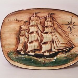 May include: A ceramic wall plaque featuring a detailed relief sculpture of a sailing ship called "The Clipper Lightning". The ship has multiple sails and is depicted on a wave with a compass rose in the upper right corner.