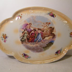 May include: Oval-shaped decorative porcelain serving dish with a scalloped edge and a painted scene of figures and a chariot in a cloudy sky. The rim has a gold-toned border and floral accents.