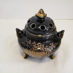 May include: Black ceramic incense burner with gold floral designs and a lid with holes. The burner has three legs and a knob on the top of the lid.
