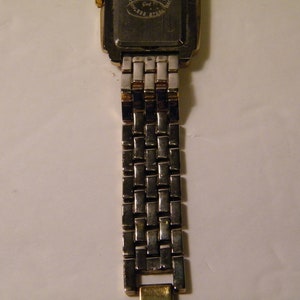 May include: A gold and silver two-tone watch with a square face and a metal band.