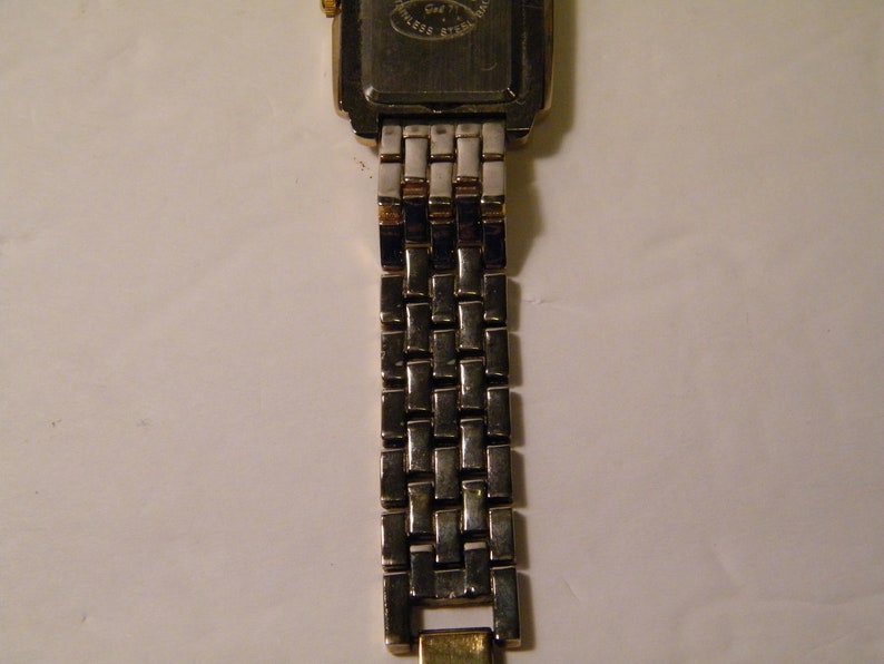 May include: A gold and silver two-tone watch with a square face and a metal band.