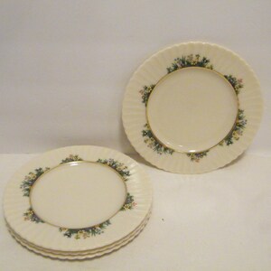 May include: Four white ceramic plates with a green and gold floral design around the rim.