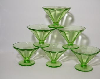 May include: Six green glass dessert dishes stacked in a pyramid shape. The dishes have a fluted design and a clear glass base.