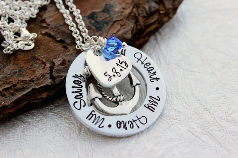 May include: A silver necklace with a pendant featuring an anchor, heart, and the words "Sailor My Heart My Hero." A blue crystal bead accents the top. The date "5.8.15" is inscribed on the heart. The necklace is on a silver chain.