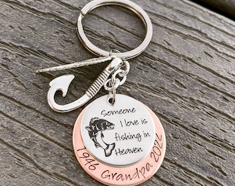 May include: Silver and copper keychain with a fishing hook charm and a round tag that reads "Someone I love is fishing in Heaven 1946 Grandpa 2022".