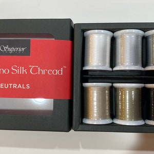 May include: A black box set of Superior Threads Kimono Silk Thread in neutral colors. The set includes six spools of thread in shades of silver, gray, and brown. The box has a red label with the product name and brand.