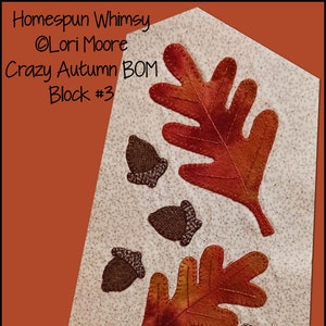 Può includere: Blocco di quilt Homespun Whimsy di Lori Moore Crazy Autumn BOM Block #3 con due foglie arancioni e rosse e quattro ghiande marroni su uno sfondo bianco con un piccolo motivo floreale.
