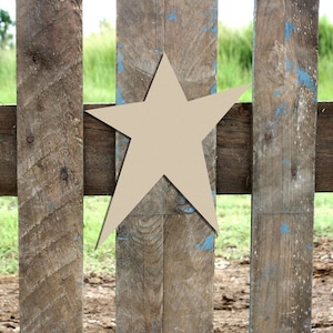 May include: A large, beige wooden star shape is attached to a weathered wooden fence. The fence is made of vertical planks with blue paint splatters.