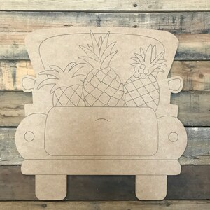 May include: A wooden cutout of a vintage truck bed filled with three pineapples. The truck is tan with etched details, including wheels and a cab. The pineapples have detailed etched textures.