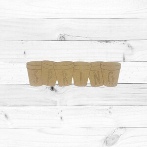 May include: A wooden craft featuring the word "SPRING" spelled out across six flower pot cutouts. The flower pots are light brown and sit on a white wooden background. The letters are cut out of the flower pots.
