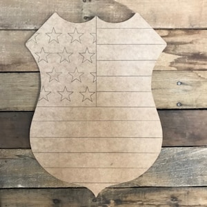May include: A wooden cutout of a police badge with an American flag design. The flag is outlined in black and has 13 stripes and 50 stars.