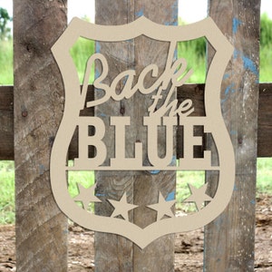 May include: Wooden cutout of a police badge with the text "Back the Blue" and three stars. The badge is brown and has a rounded shape.