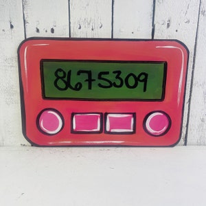 May include: A red wooden door hanger shaped like a vintage calculator with a green display showing the number 8675309. The calculator has four pink buttons.