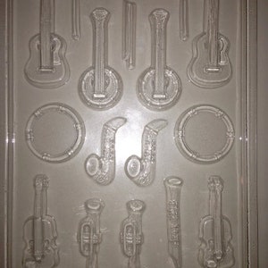 May include: A clear plastic mold with cavities shaped like musical instruments. The mold includes guitars, banjos, saxophones, trumpets, a clarinet, a violin, and a drum. The text "LIFE OF THE PARTY 00606 FDA 430" is visible.
