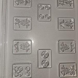May include: Clear plastic mold for making game pieces. The mold features various rectangular and circular cavities with embossed Chinese characters and circular designs. The text "LIFE OF THE PARTY M 260 - B" is at the bottom.