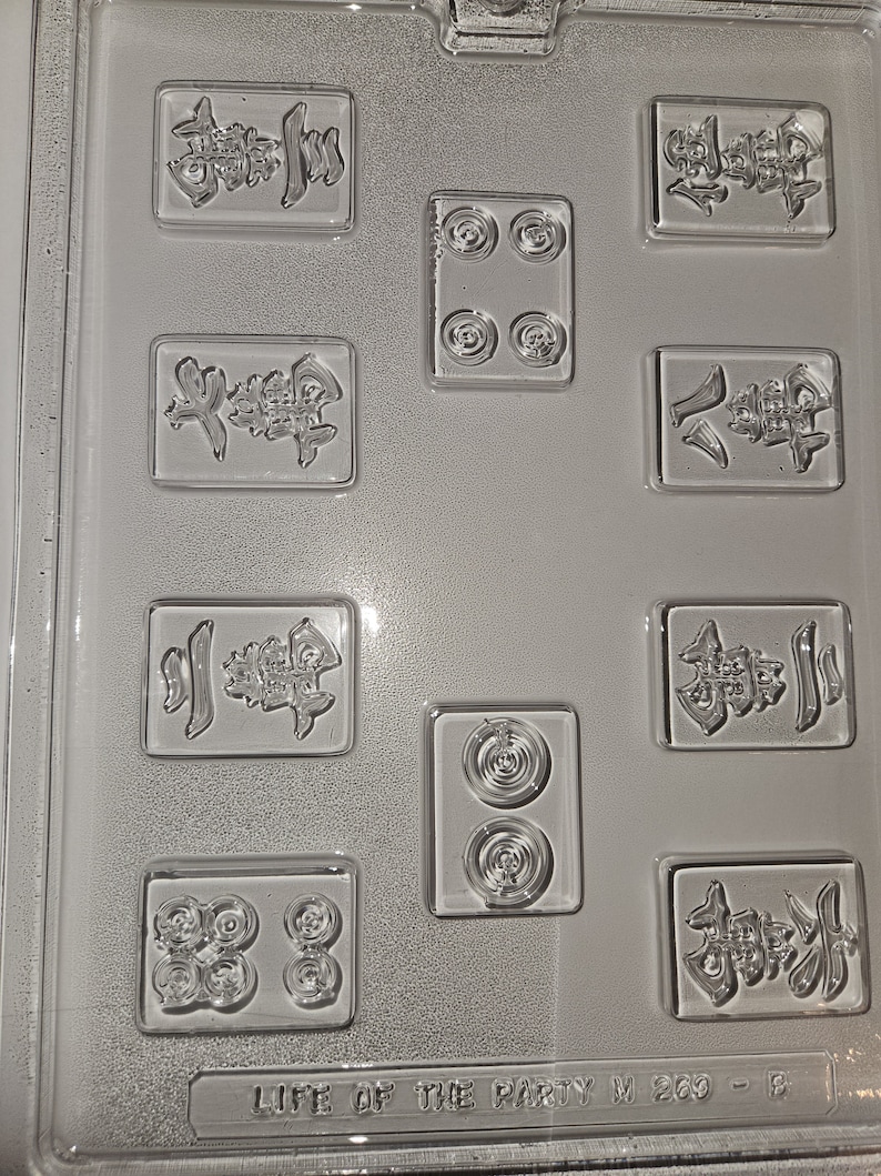 May include: Clear plastic mold for making game pieces. The mold features various rectangular and circular cavities with embossed Chinese characters and circular designs. The text "LIFE OF THE PARTY M 260 - B" is at the bottom.