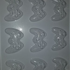 May include: A clear plastic mold with nine gamepad-shaped cavities. Each cavity has detailed button and joystick impressions. The text "LIFE OF THE PARTY K 180" is visible at the bottom of the mold. Ideal for crafting themed treats.