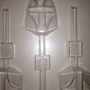 May include: A clear plastic mold for making candy lollipops shaped like a Star Wars Boba Fett helmet. The mold has three cavities, each with a stick holder.