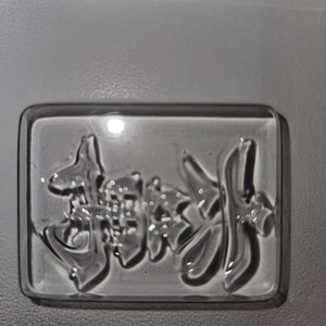 May include: A clear, rectangular mold with embossed Japanese characters. The characters are in a stylized font and appear to be for a food item. The mold is made of a clear, glossy material.