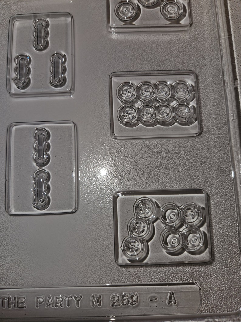 May include: Clear plastic candy mold with various shaped cavities. The mold includes rectangular and circular shapes, with the text "THE PARTY M 269 - A" at the bottom. The cavities are designed for creating candies or chocolates.