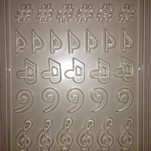 May include: A clear plastic mold for making chocolate candy. The mold has 20 cavities, each shaped like a different musical note. The mold is labeled "Life of the Party 08886 FDA App J."