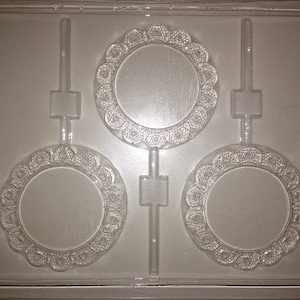 May include: A clear plastic mold with three round cavities for making chocolate lollipops. Each cavity has a decorative design around the edge. The mold has a stick holder for each lollipop. The mold is labeled "LIFE OF THE PARTY 08888 FDA APPL'd GT".