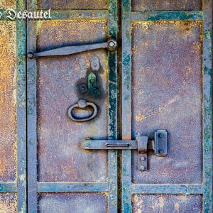 May include: A close-up of a rusty metal door with a metal handle and a latch. The door is painted in shades of blue and green, with a brown and yellow patina.