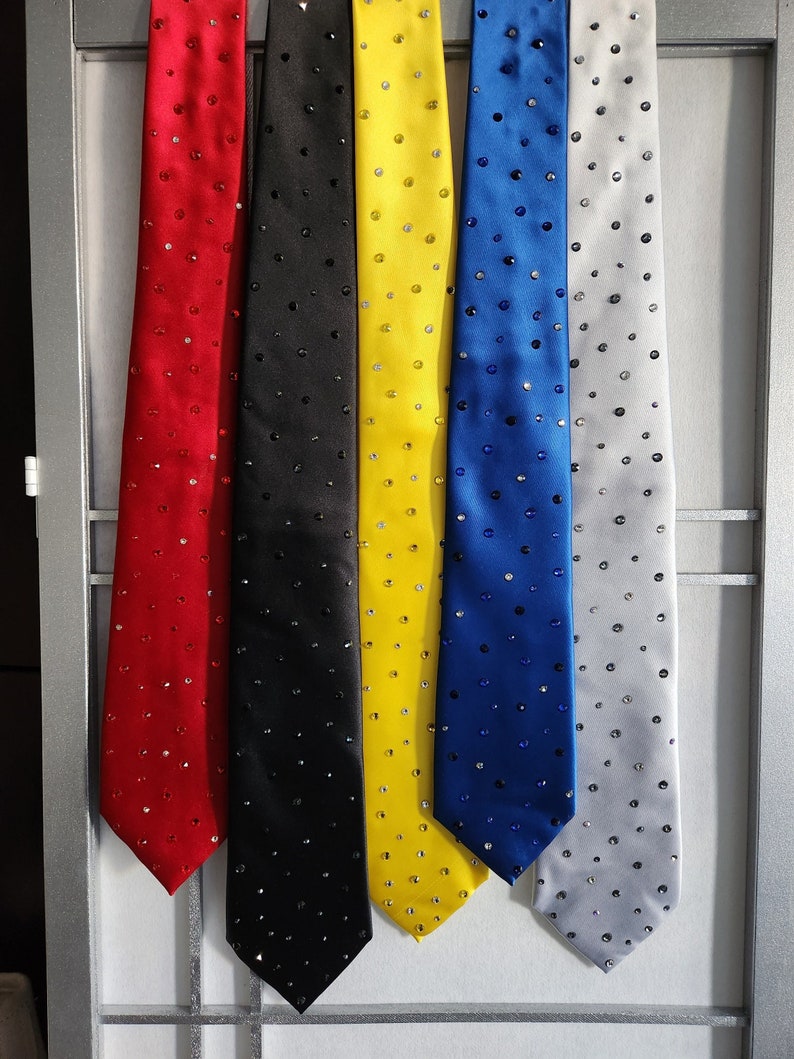 Row of hanging neckties decorated in rhinestones. From left to right: red, black, yellow, royal blue, silver.