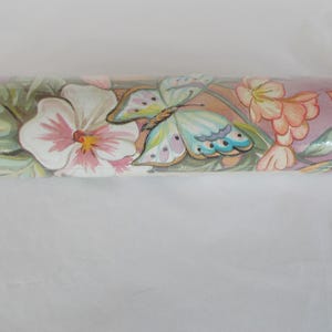 May include: Rolled wallpaper featuring a repeating pattern of butterflies, flowers, and foliage. The design includes white and pink flowers, a butterfly with blue and yellow wings, and green leaves, all set against a pink background.