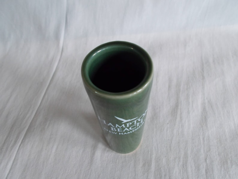 May include: A green ceramic shot glass with white text that reads "Hampton Beach New Hampshire".