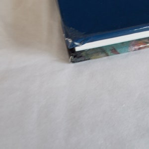 May include: The top of a blue hardcover book with a white spine and a colorful patterned cover underneath.