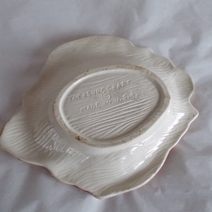 May include: White ceramic serving dish with a scalloped edge. The bottom of the dish has a brown oval label with the text "Treasure Craft Made in U.S.A."