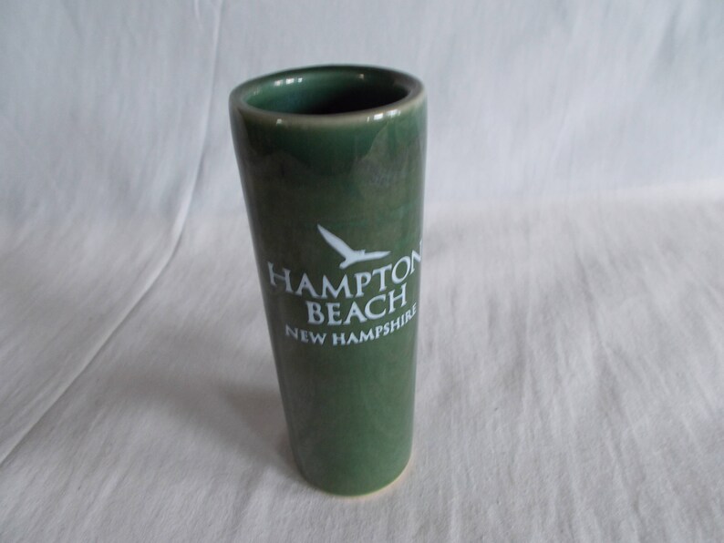 May include: A green ceramic shot glass with a white bird and the text "Hampton Beach New Hampshire".