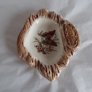 May include: A small, white ceramic dish shaped like a tree stump with a brown butterfly design and the text "Hampton Beach New Hampshire".
