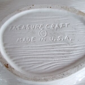 May include: White ceramic dish with a woodgrain texture on the bottom. The dish is marked "Treasure Craft" with a copyright symbol and "Made in U.S.A."
