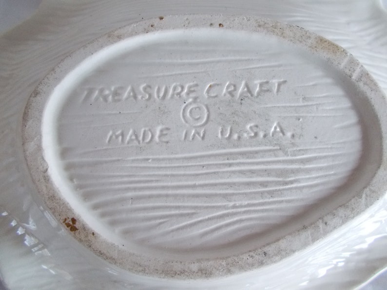 May include: White ceramic dish with a woodgrain texture on the bottom. The dish is marked "Treasure Craft" with a copyright symbol and "Made in U.S.A."