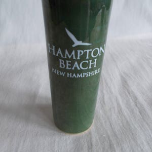 May include: A green ceramic vase with a white silhouette of a bird and the text "Hampton Beach New Hampshire".