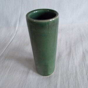 May include: A green ceramic vase with a smooth, rounded exterior. The vase is cylindrical in shape and has a simple, elegant design.