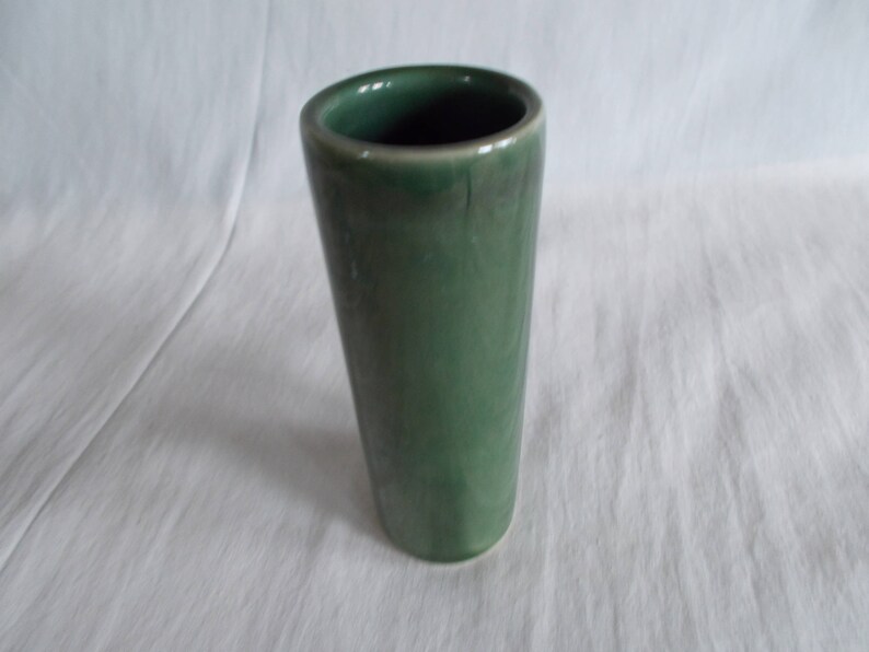May include: A green ceramic vase with a smooth, rounded exterior. The vase is cylindrical in shape and has a simple, elegant design.